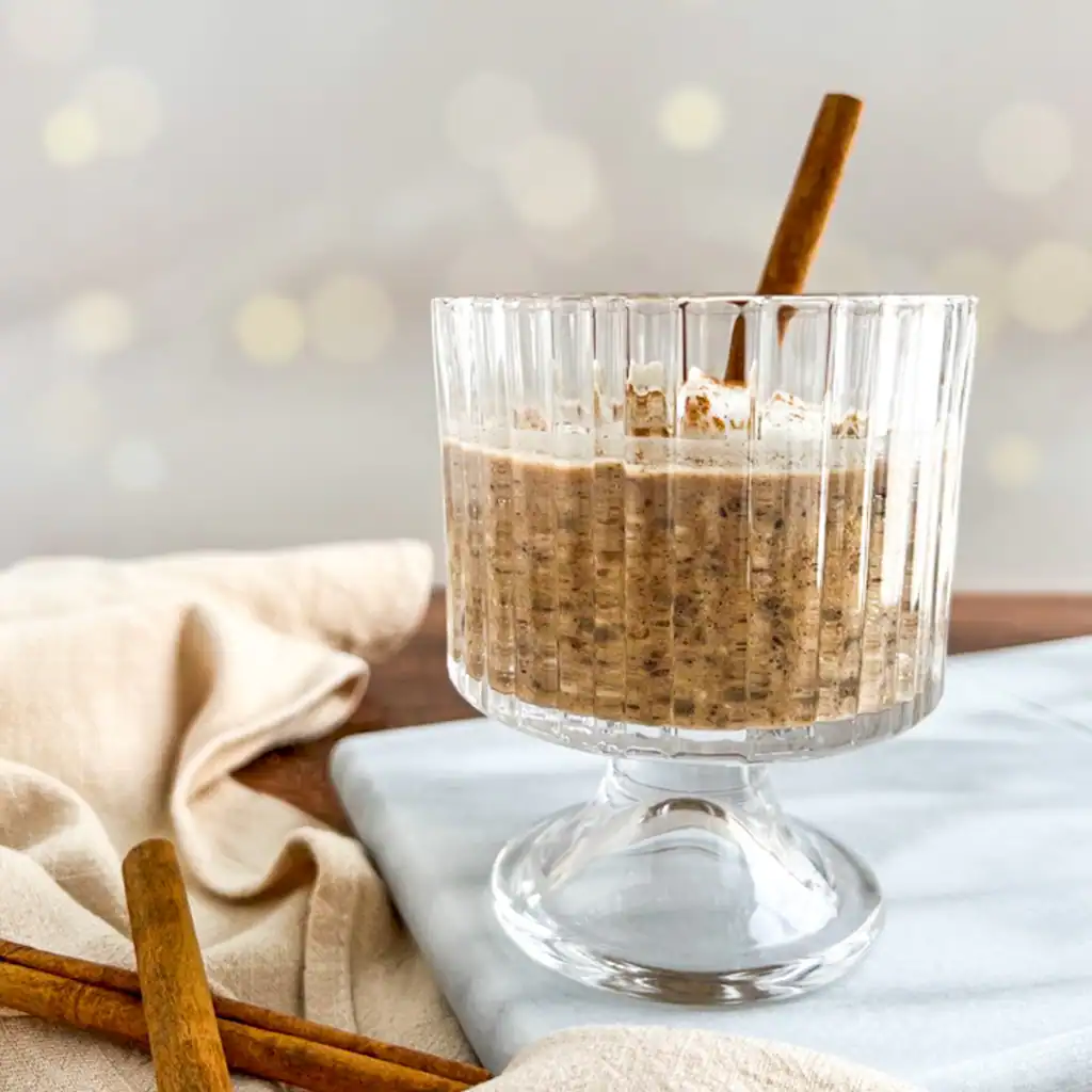 Chai spice overnight oats in a glass with cinnamon sticks on the side.