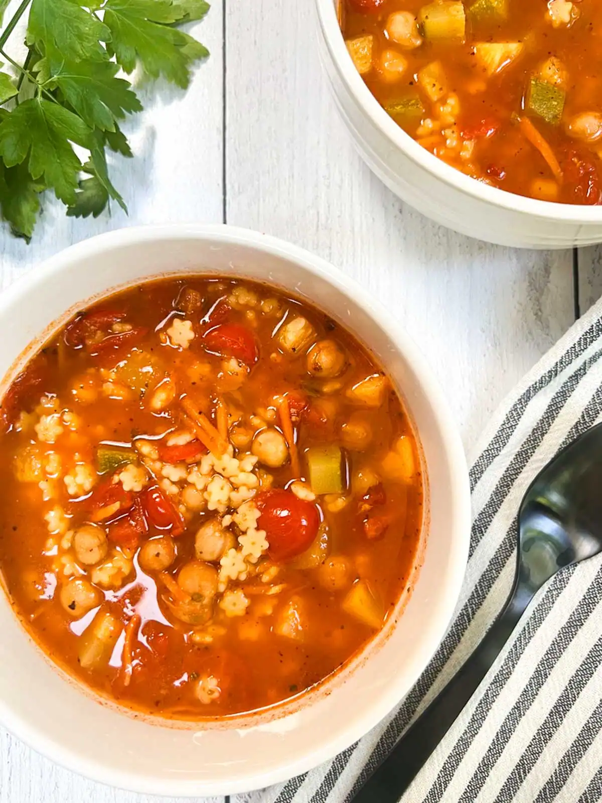Easy vegan minestrone soup in white bowls on a white wooden surface with fresh parsley.