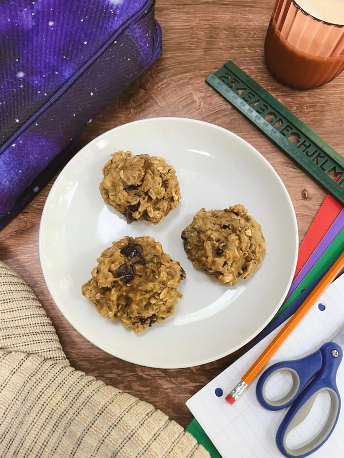 Healthy vegan breakfast cookies on a white plate with school supplies and a backpack nearby.