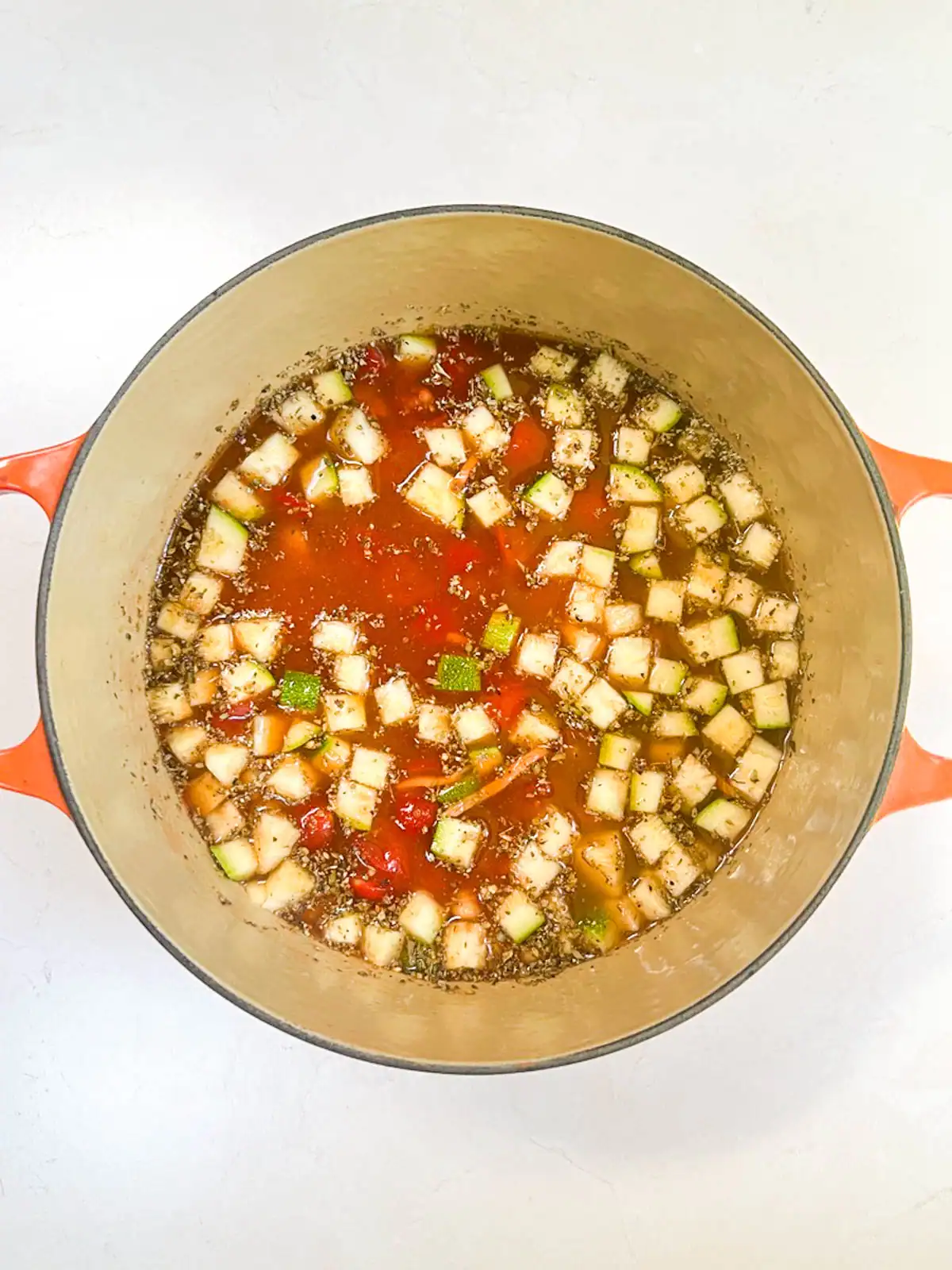 Vegan minestrone vegetable soup with zucchini, tomatoes, and herbs in a cooking pot.