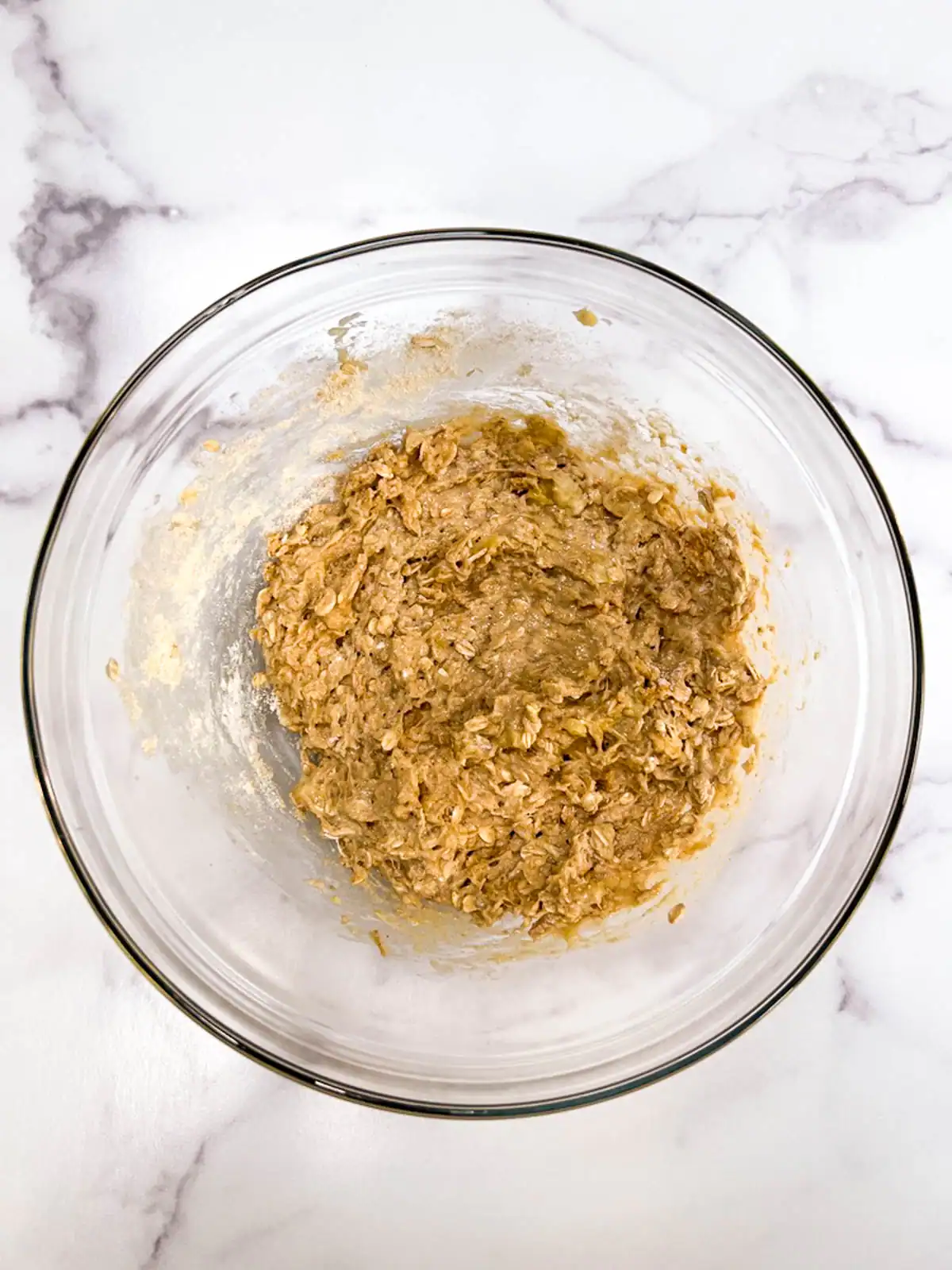 Creamy vegan oatmeal cookie dough in a glass bowl on a white marble surface.