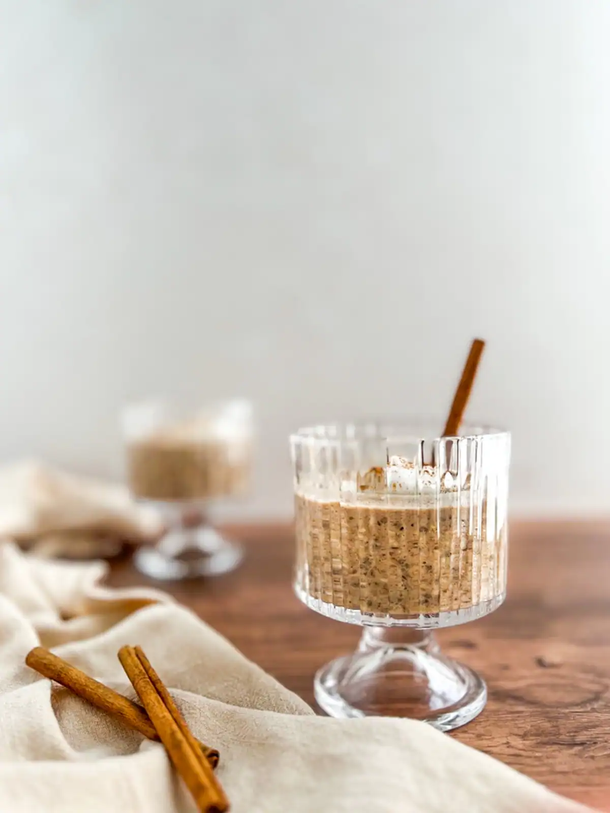 Chai spice overnight oats in an elegant glass with cinnamon sticks for garnish.