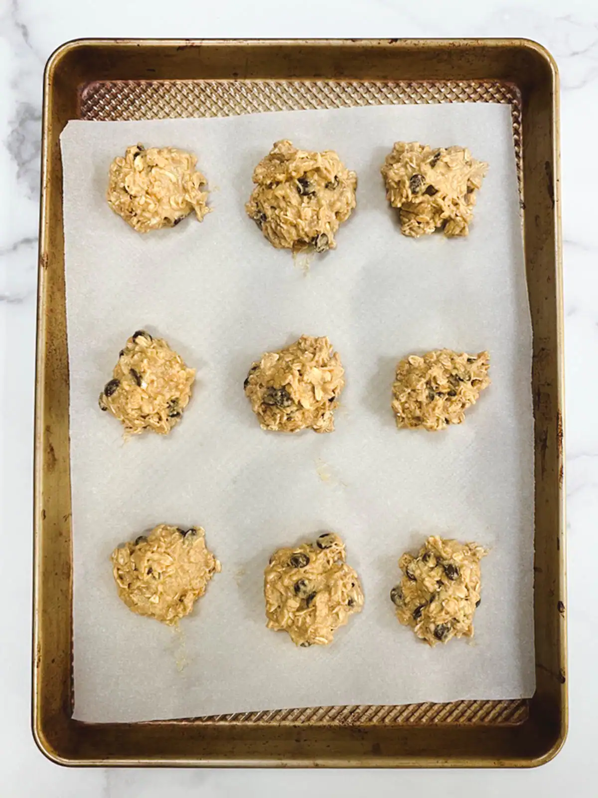 Oatmeal chocolate chip cookie dough scoops on a baking sheet ready to bake.