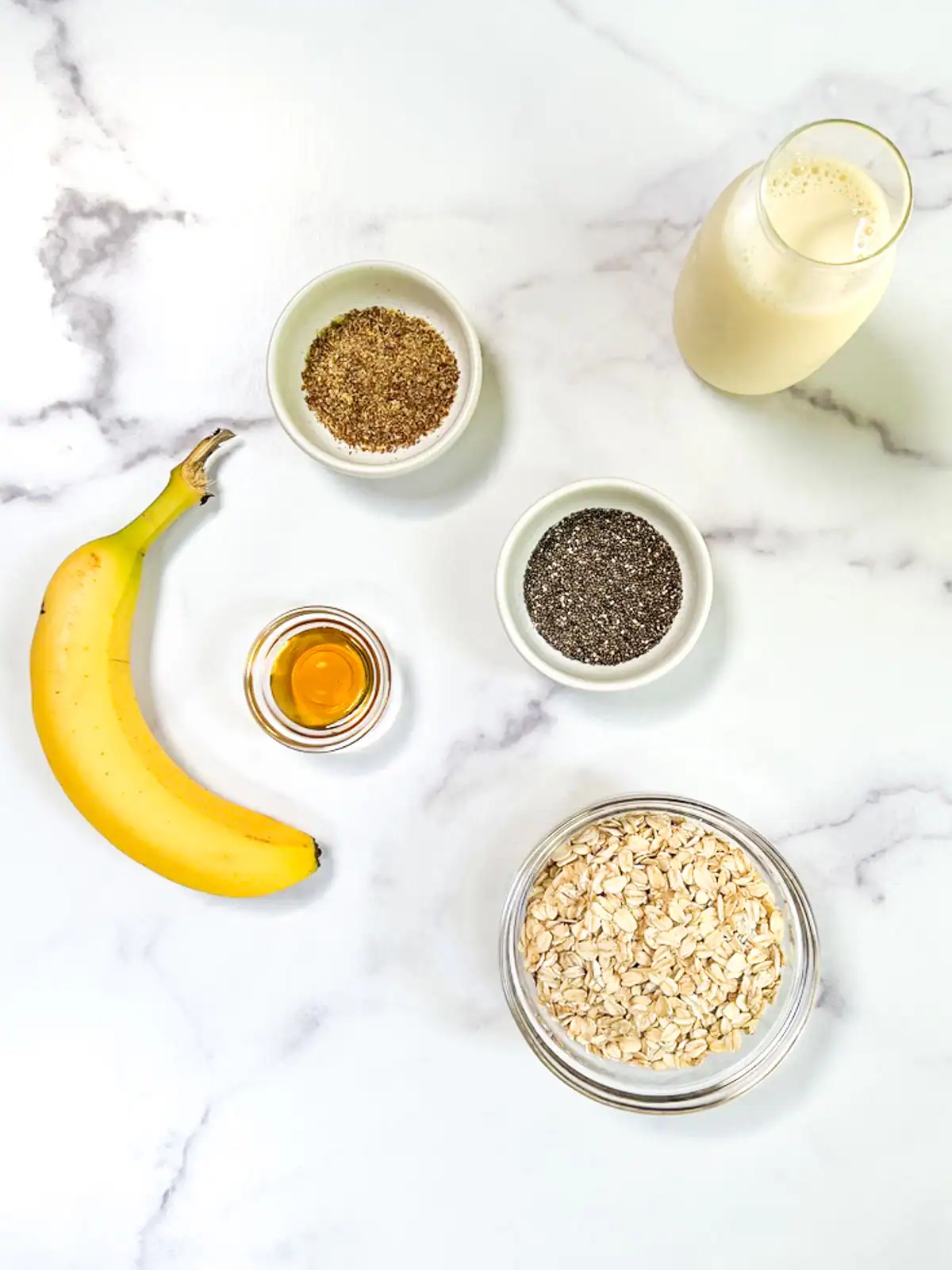 Ingredients for easy plant-based overnight oats, including chia seeds, oats, and plant-based milk, on a marble surface.