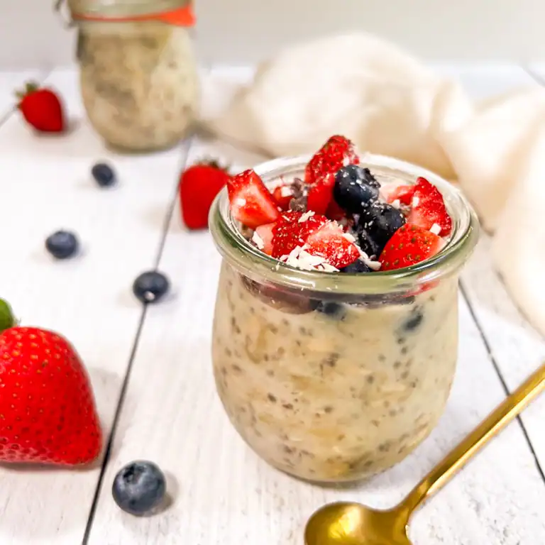 Fresh vegan overnight oats with strawberries and blueberries, served in a glass jar.