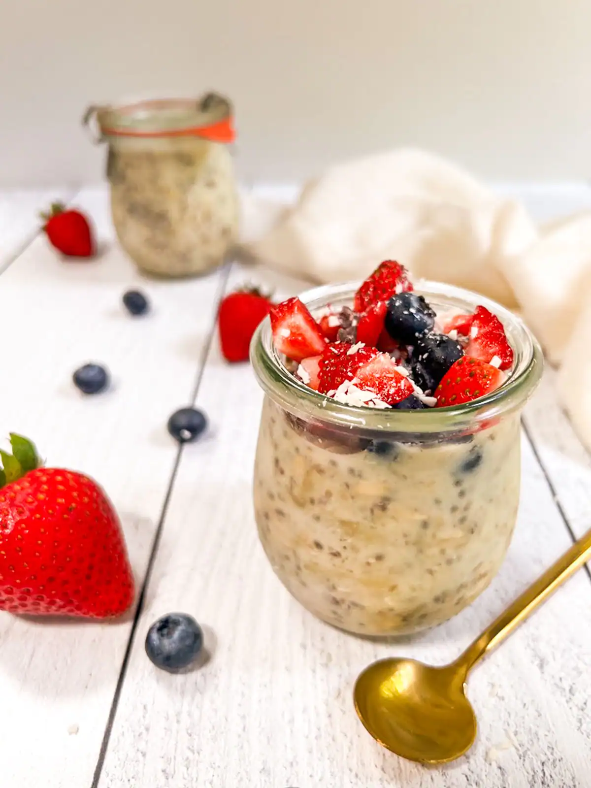 Creamy plant-based overnight oats topped with mixed berries, strawberries, blueberries, and shredded coconut, served in a glass jar.