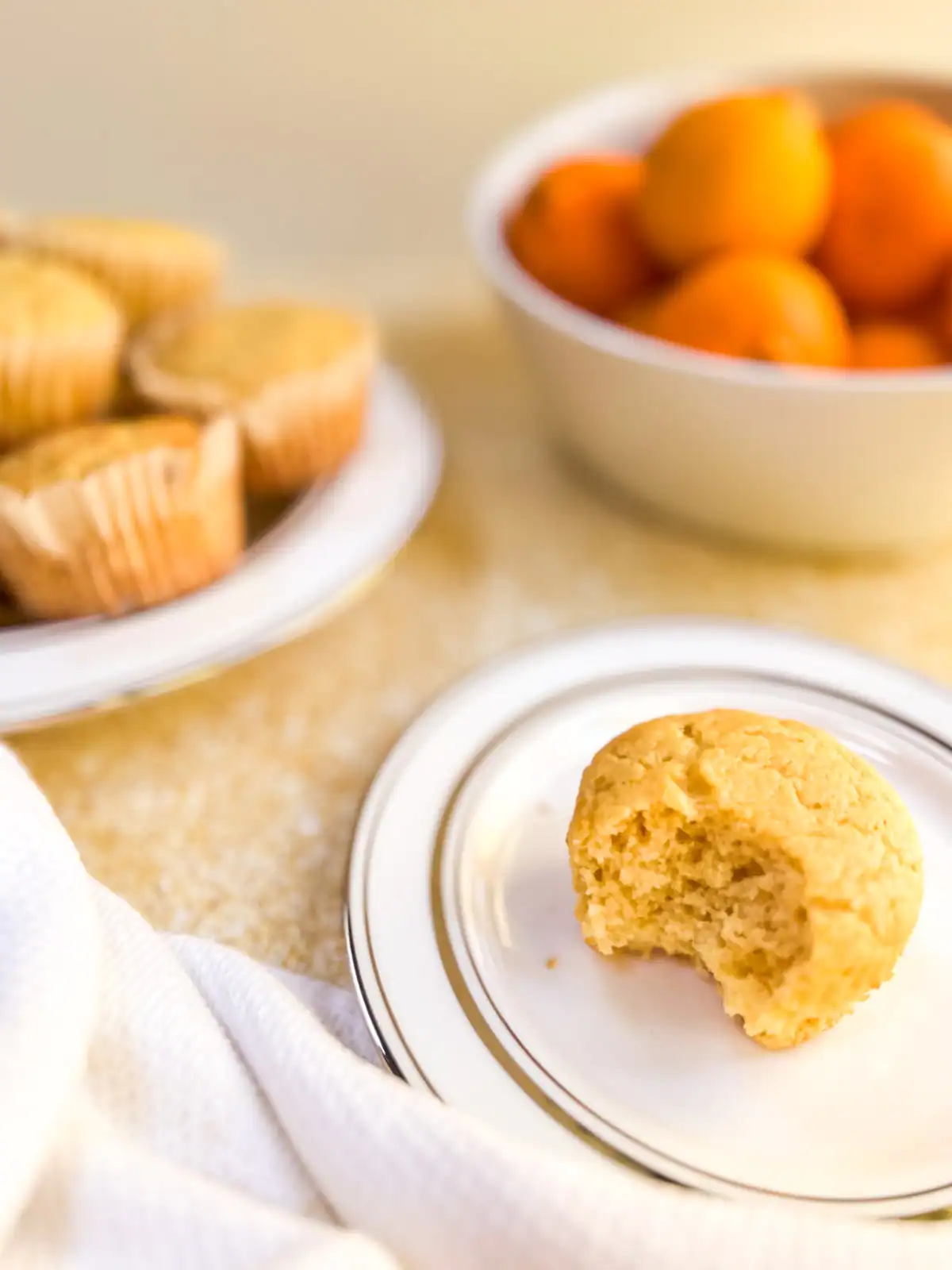 Fluffy orange vanilla muffin with a bite taken out, served on a white plate.
