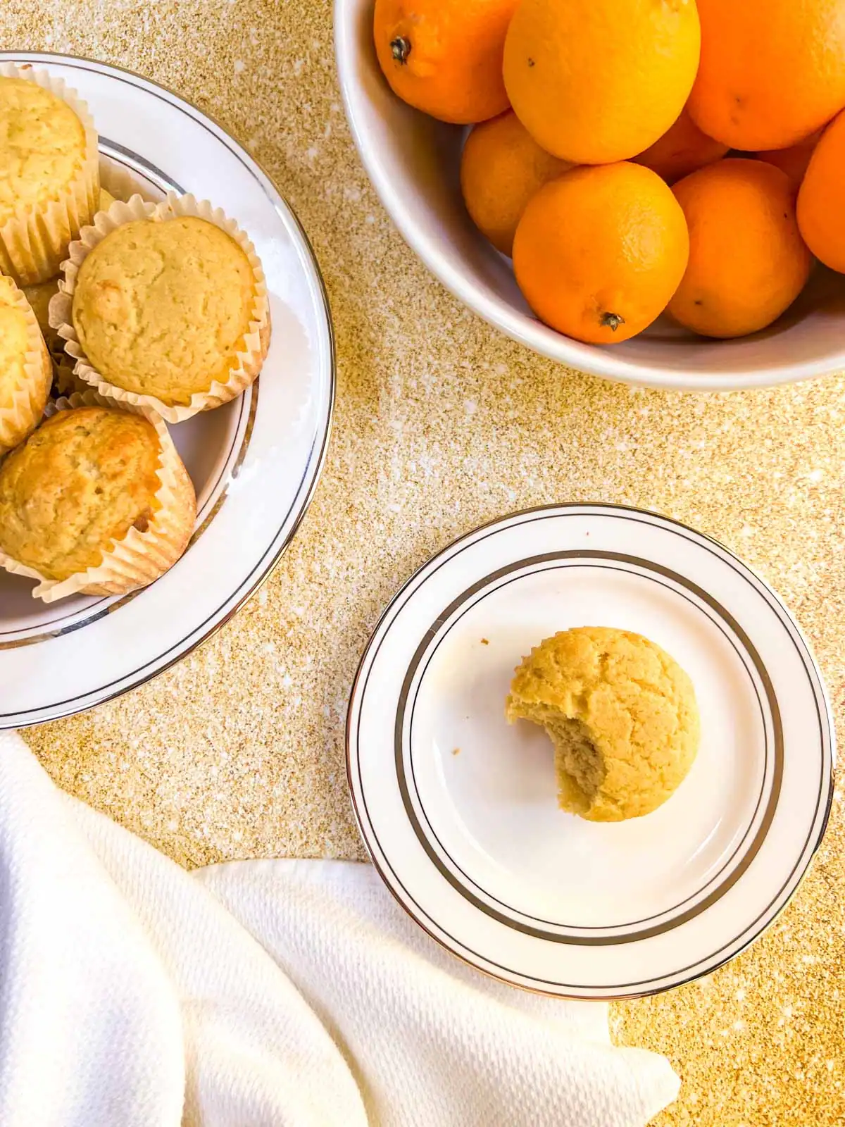 Vegan orange vanilla muffins on a white plate with fresh oranges in a bowl.