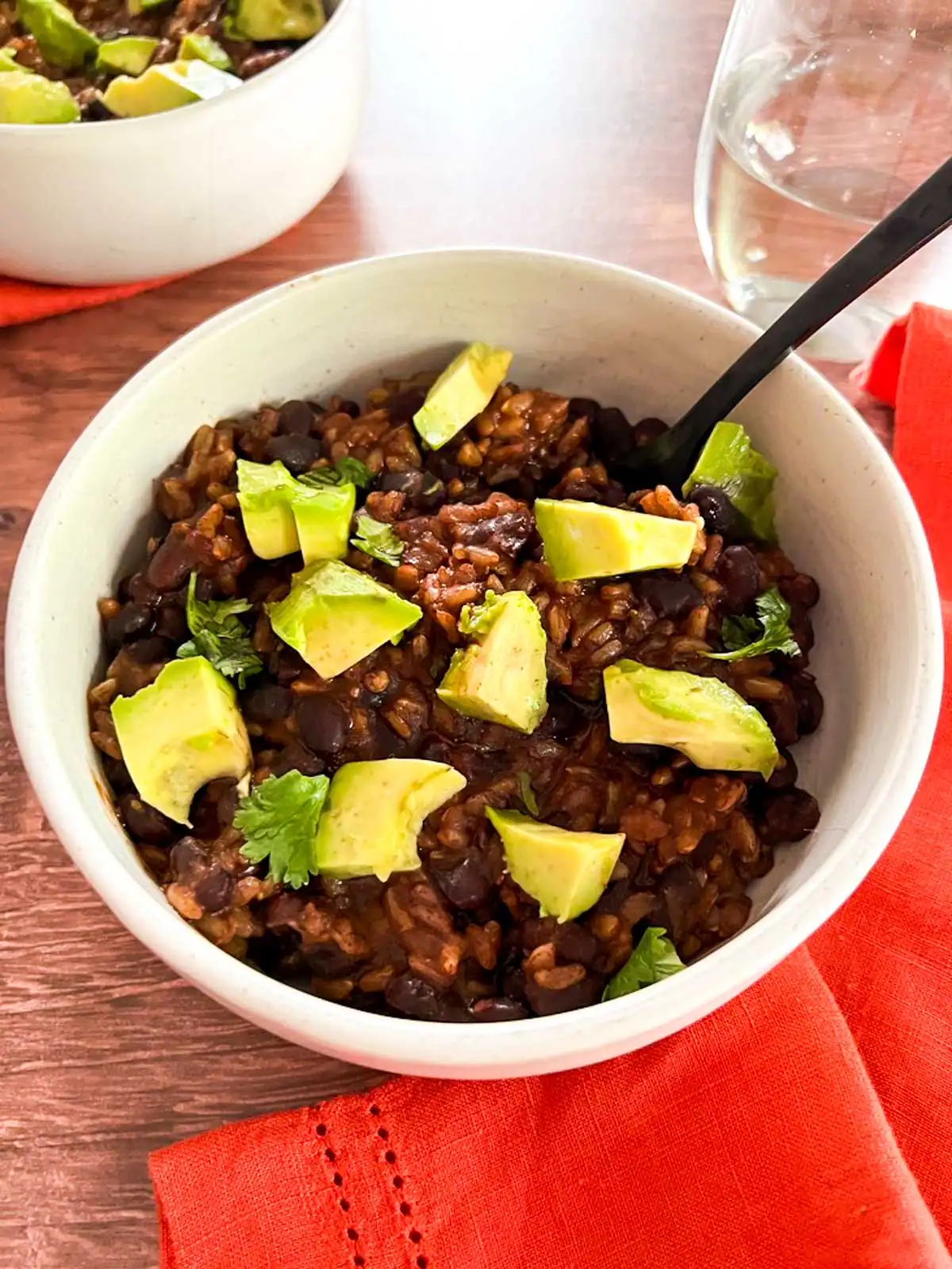Creamy vegan black bean and rice bowl garnished with avocado and cilantro on wooden table.