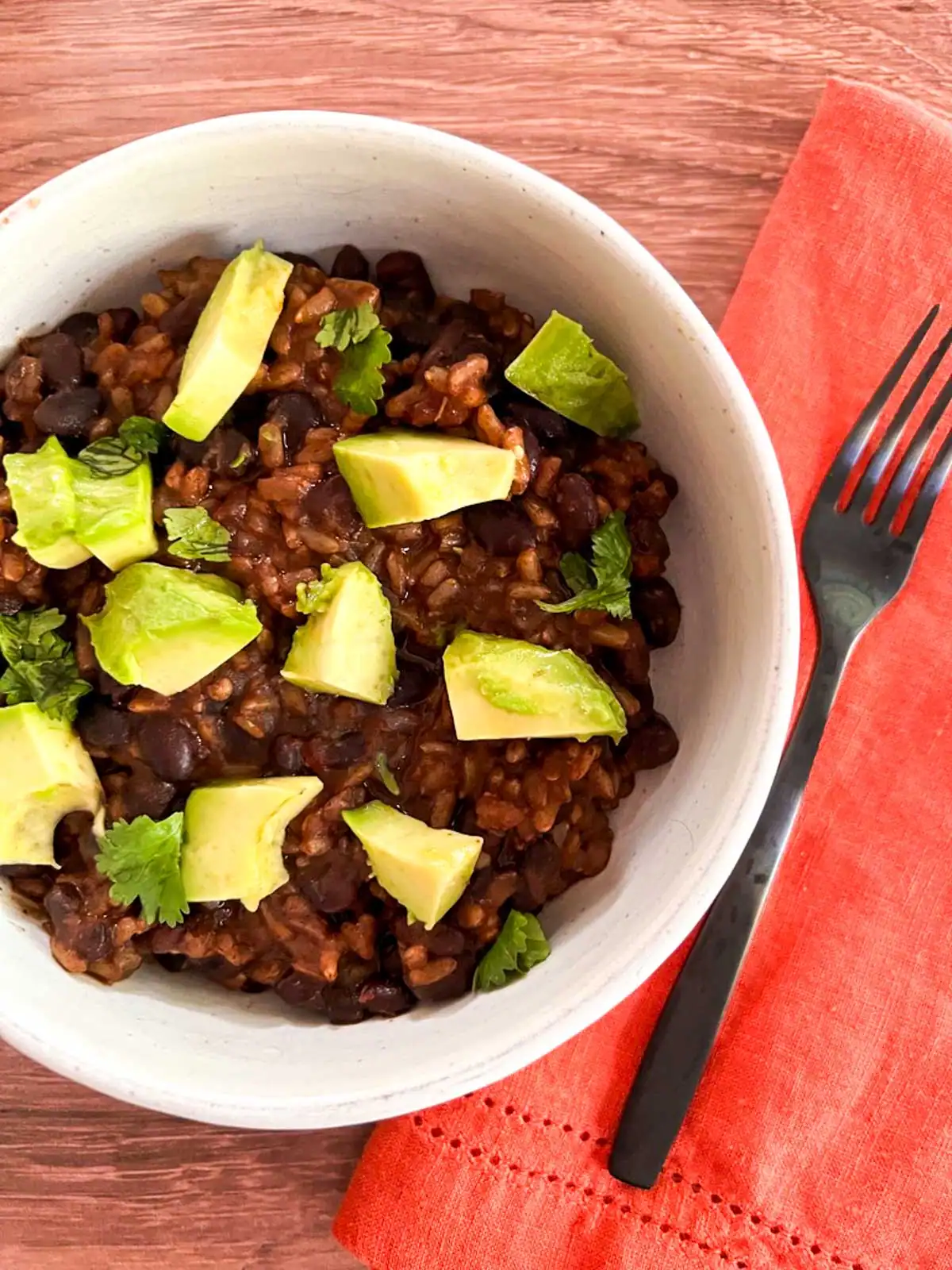 Black bean and rice vegan bowl with avocado and cilantro on a wooden table.