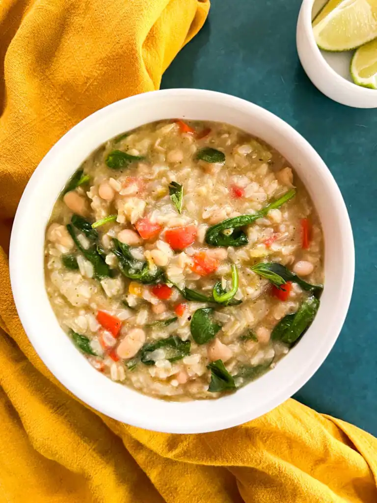 Creamy Instant Pot vegan green curry rice in a white bowl next to a yellow cloth and lime wedges.