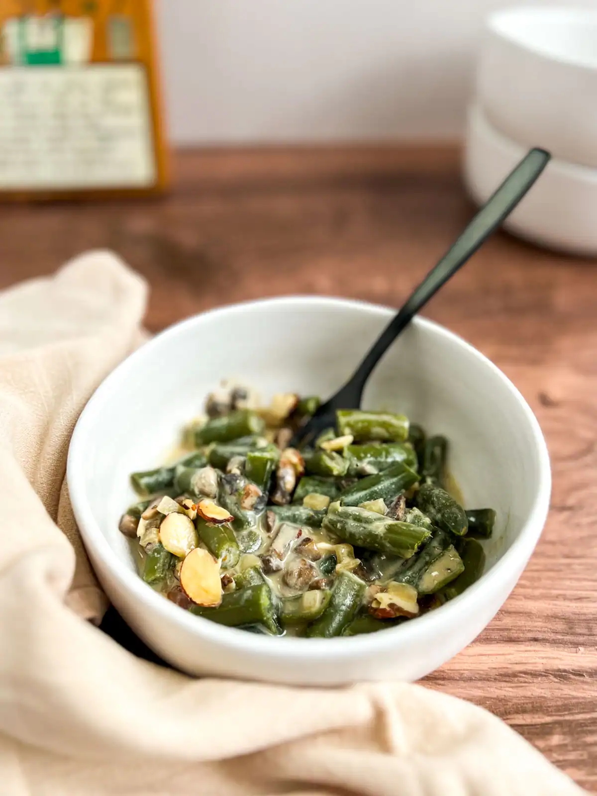 Serving of creamy vegan green bean casserole with crunchy almond topping in a white bowl.
