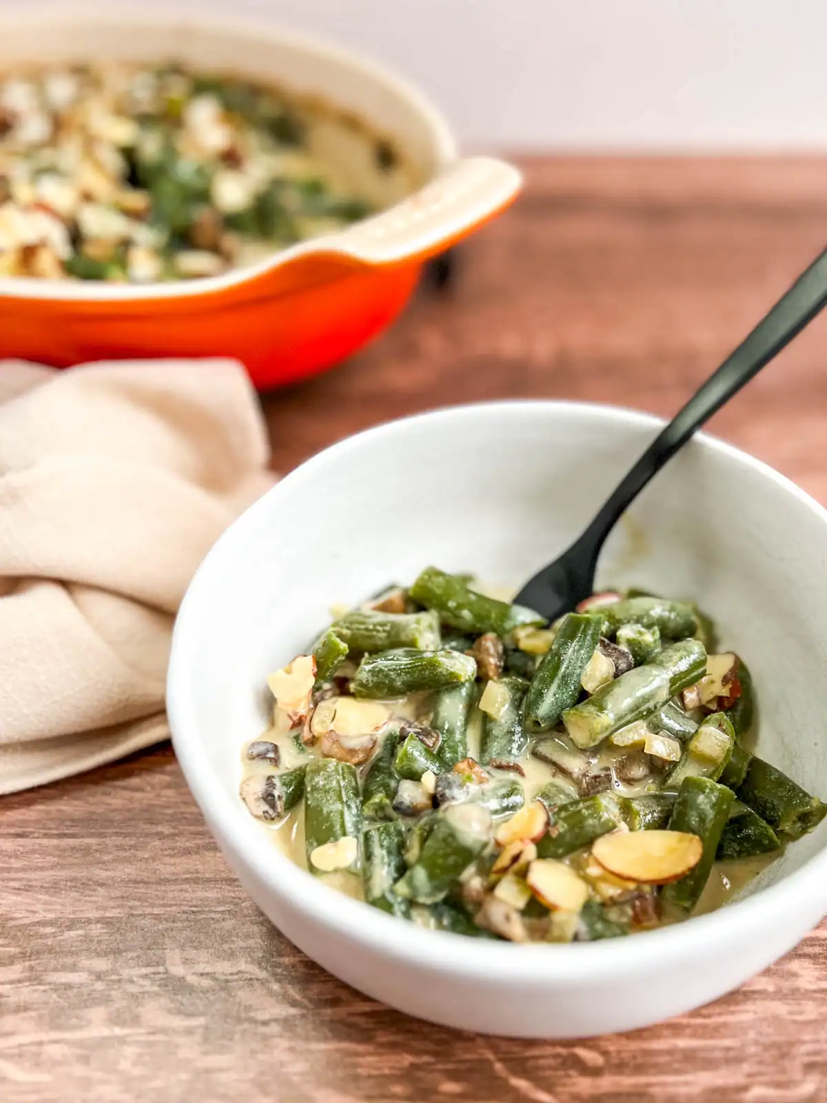 Serving of vegan green bean casserole with crunchy almond topping in a white bowl.