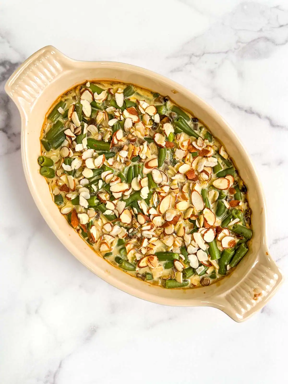 Vegan green bean casserole with almond topping in a casserole dish.