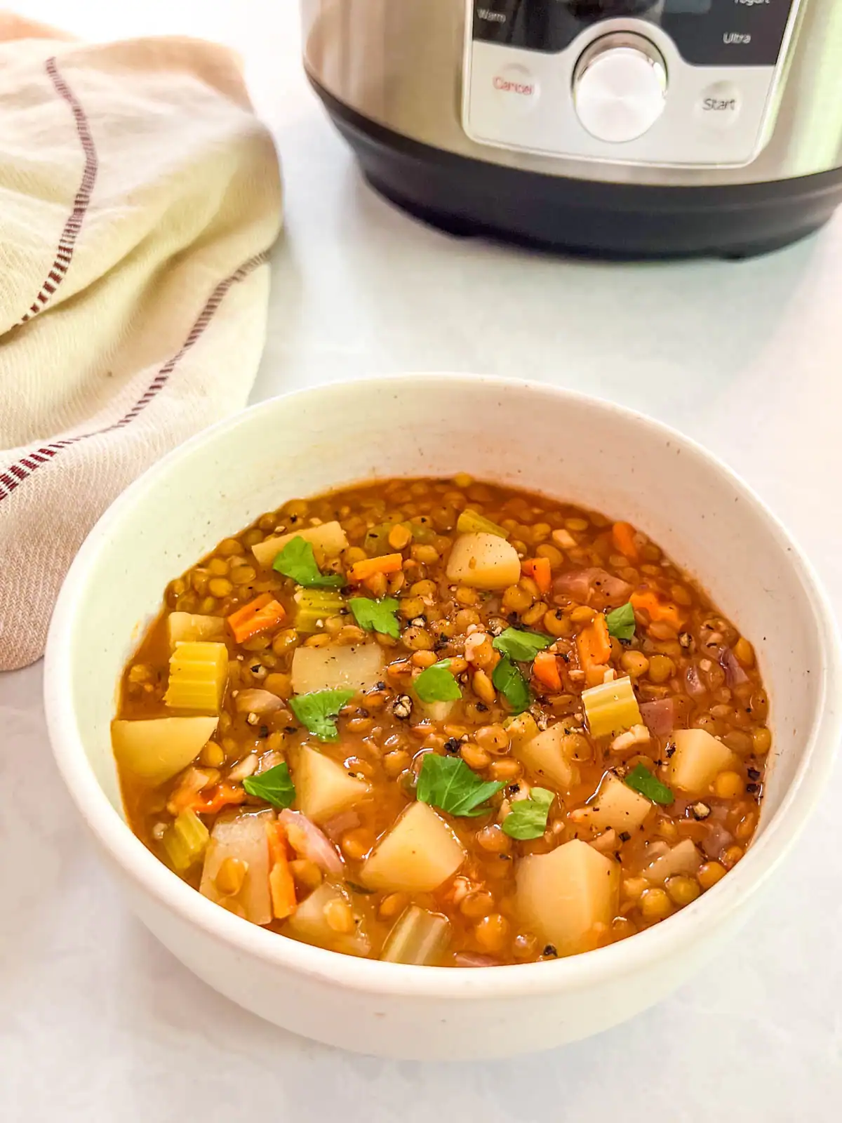 Instant Pot vegan lentil soup in a white bowl with vegetables, served on a kitchen counter.