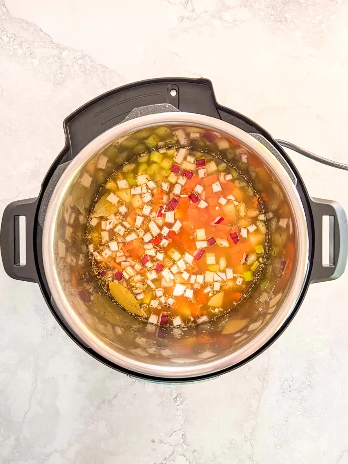 Instant Pot containing ingredients for vegan lentil soup with liquids added.