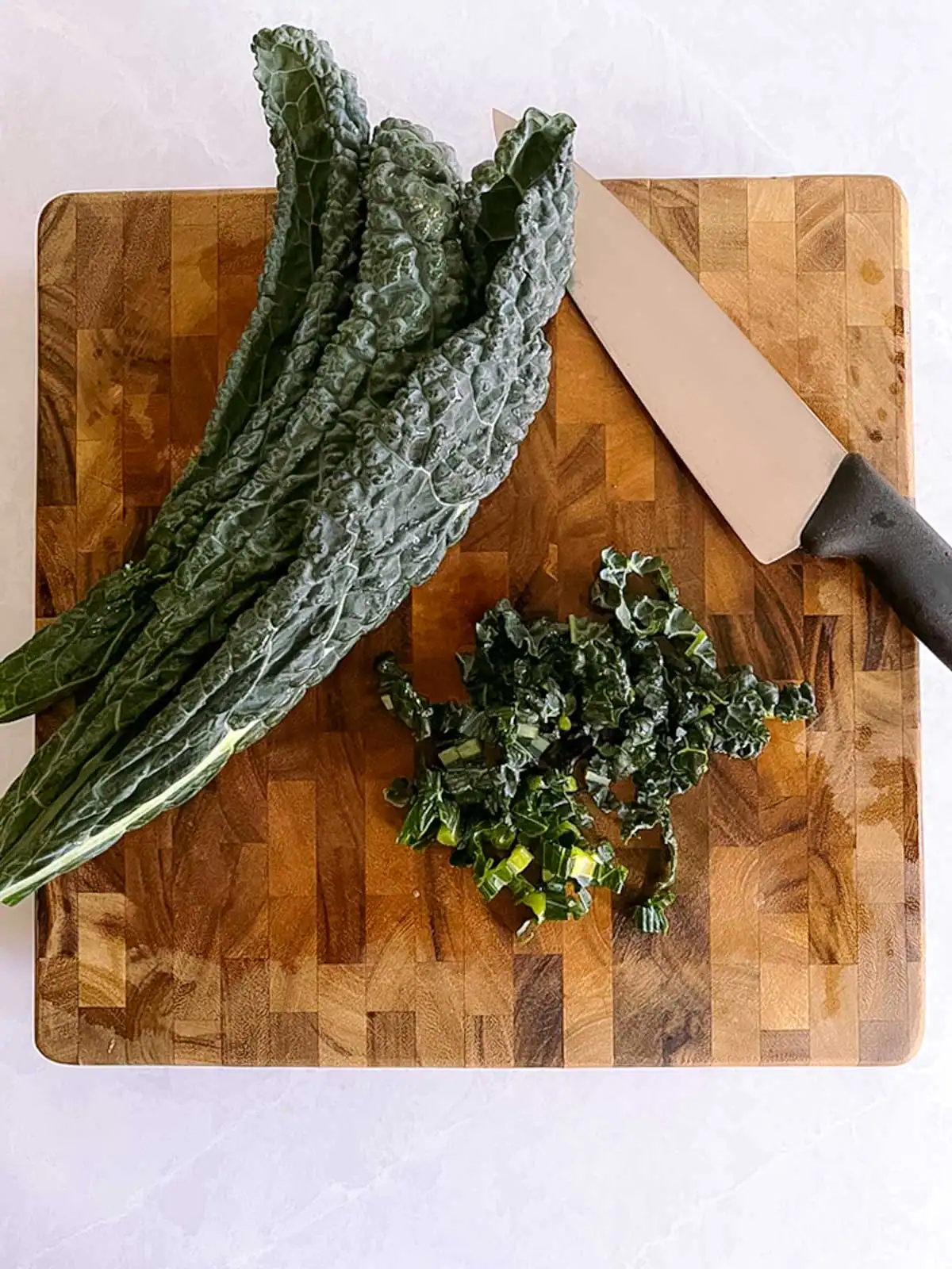 Fresh kale on a wooden cutting board with a chef's knife.