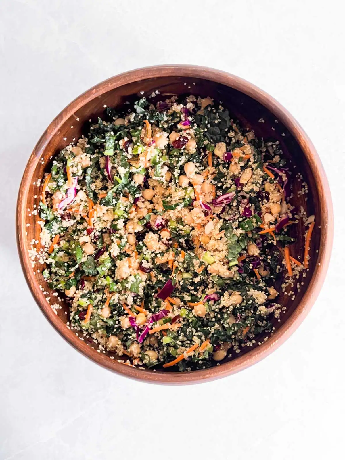 Vegan quinoa kale salad with chickpeas and cranberries in wooden bowl.