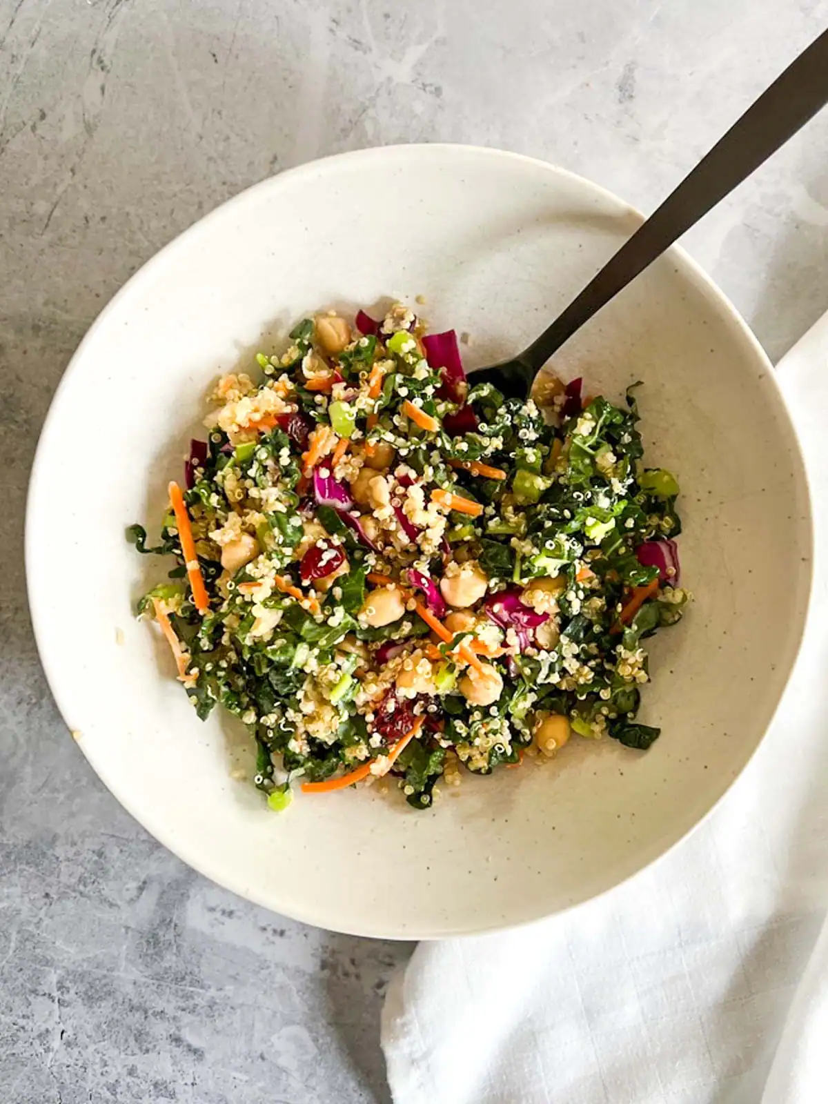 Vegan quinoa kale salad with chickpeas and cranberries in a white bowl.