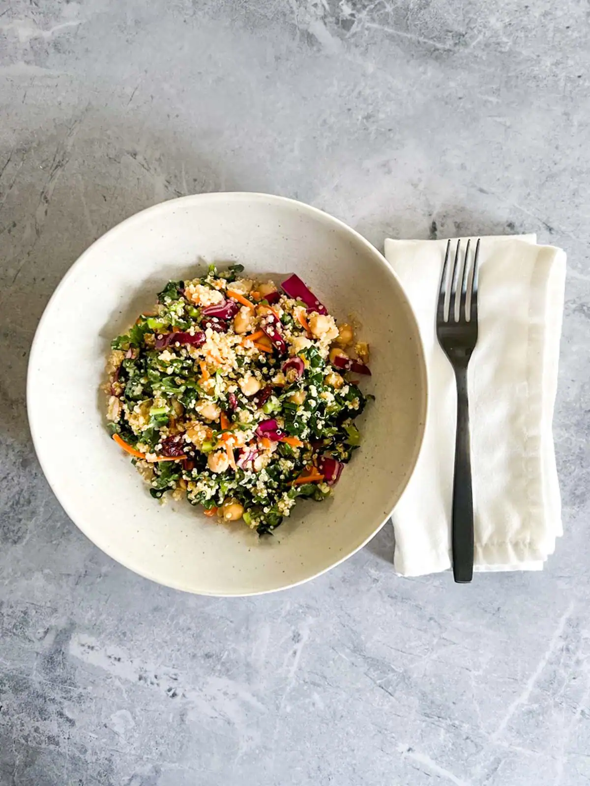 Vegan quinoa kale salad with chickpeas and cranberries in a white bowl.
