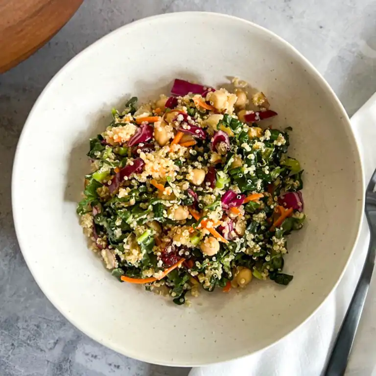 Fresh vegan quinoa kale salad with chickpeas and cranberries in a white bowl.