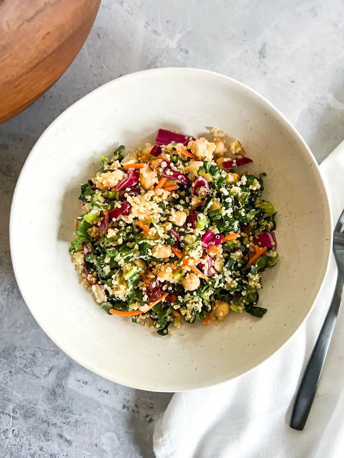 Fresh vegan quinoa kale salad with chickpeas and cranberries in a white bowl.