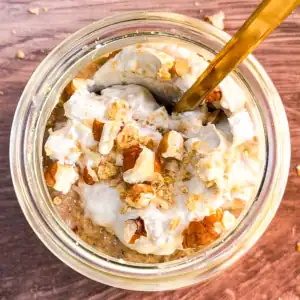 Blended vegan pumpkin spice overnight oats in a glass jar topped with crushed nuts and coconut whipped cream.
