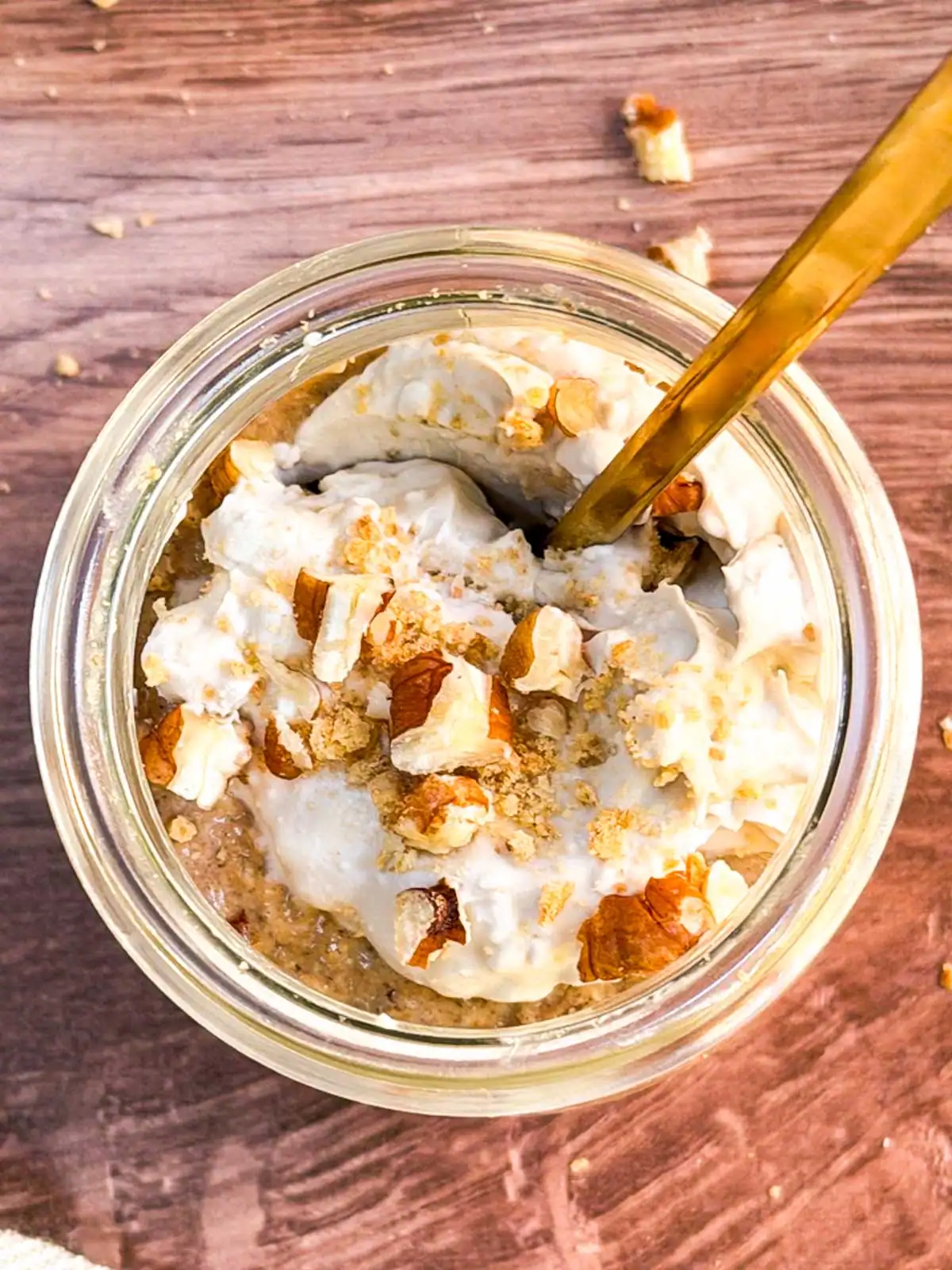 Blended vegan pumpkin spice overnight oats in a glass jar topped with crushed nuts and coconut whipped cream.