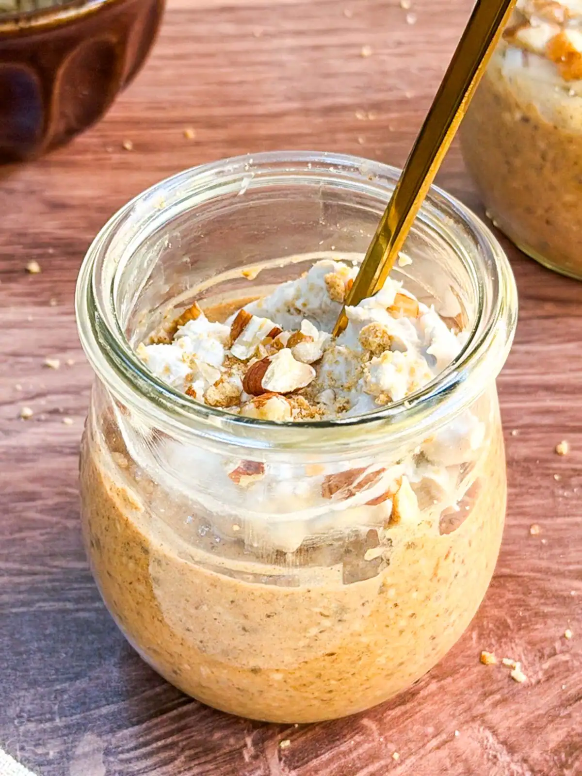 Blended vegan pumpkin spice overnight oats in a glass jar topped with crushed nuts and coconut whipped cream.