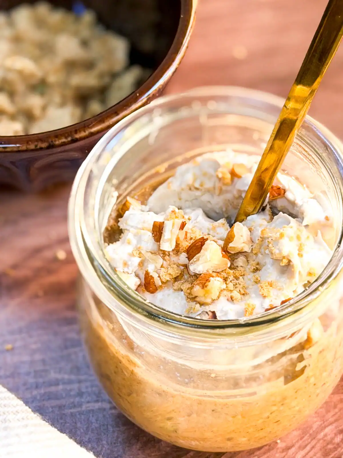 Blended vegan pumpkin spice overnight oats in a glass jar topped with crushed nuts and coconut whipped cream.