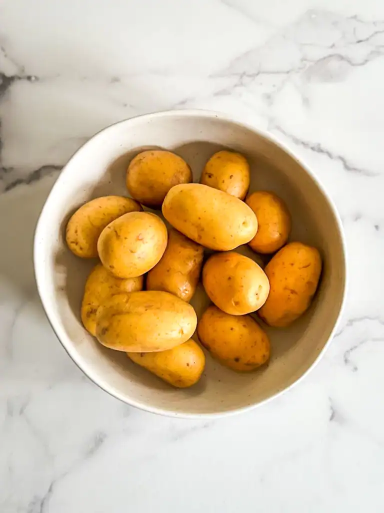 Baby gold potatoes in a white bowl on a marble surface.