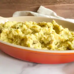 Creamy vegan mashed potatoes in an orange serving dish.