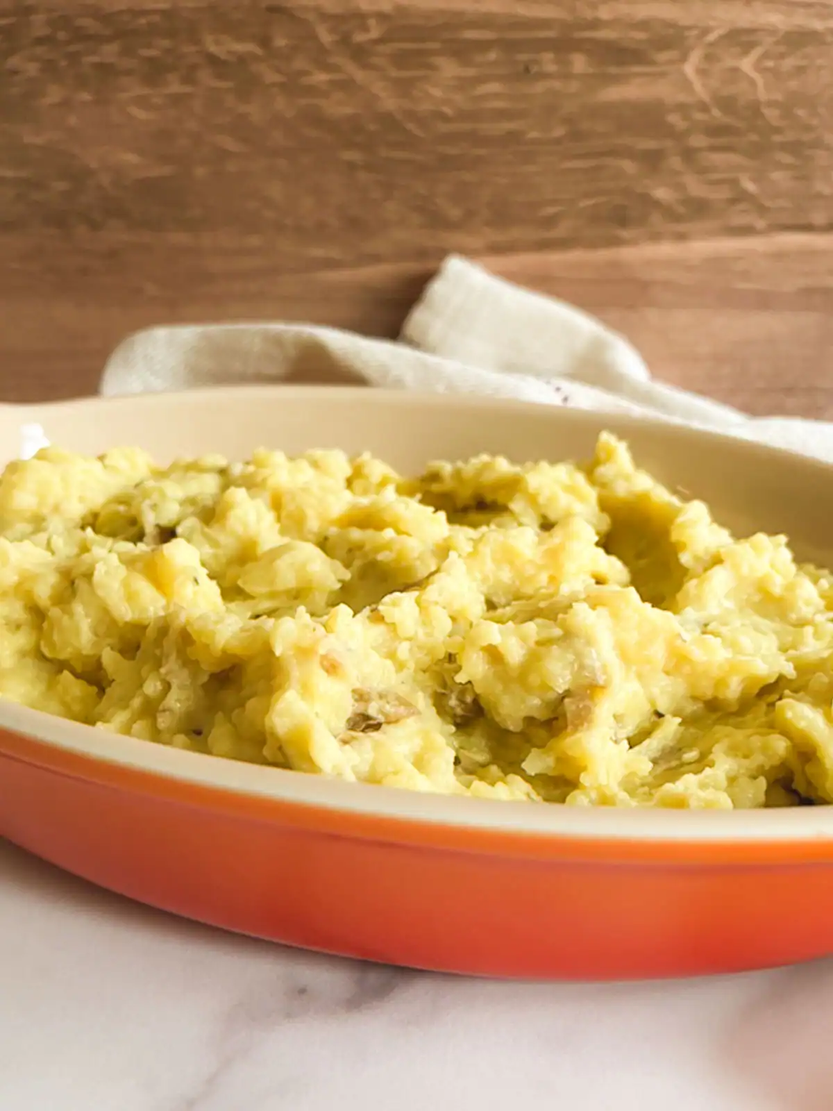 Creamy vegan mashed potatoes in an orange serving dish.