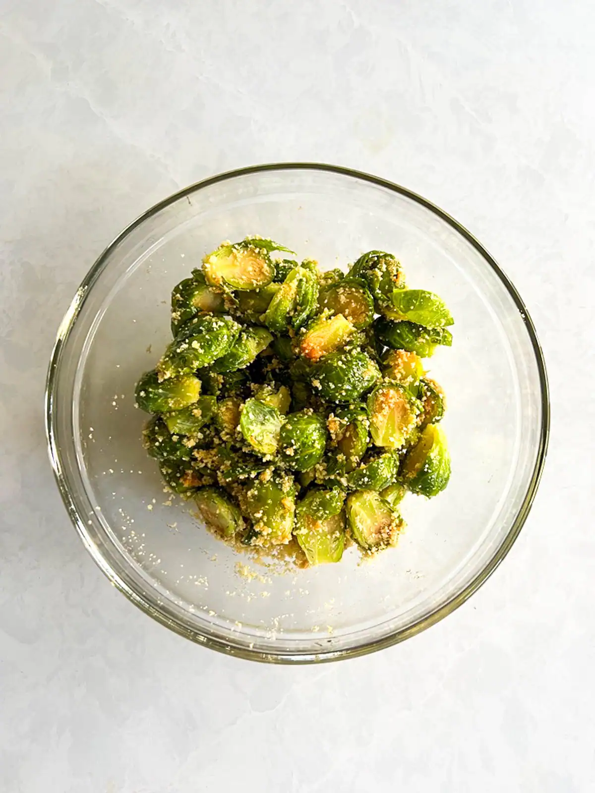 Brussels sprouts tossed with breadcrumbs and seasoning in a glass bowl.