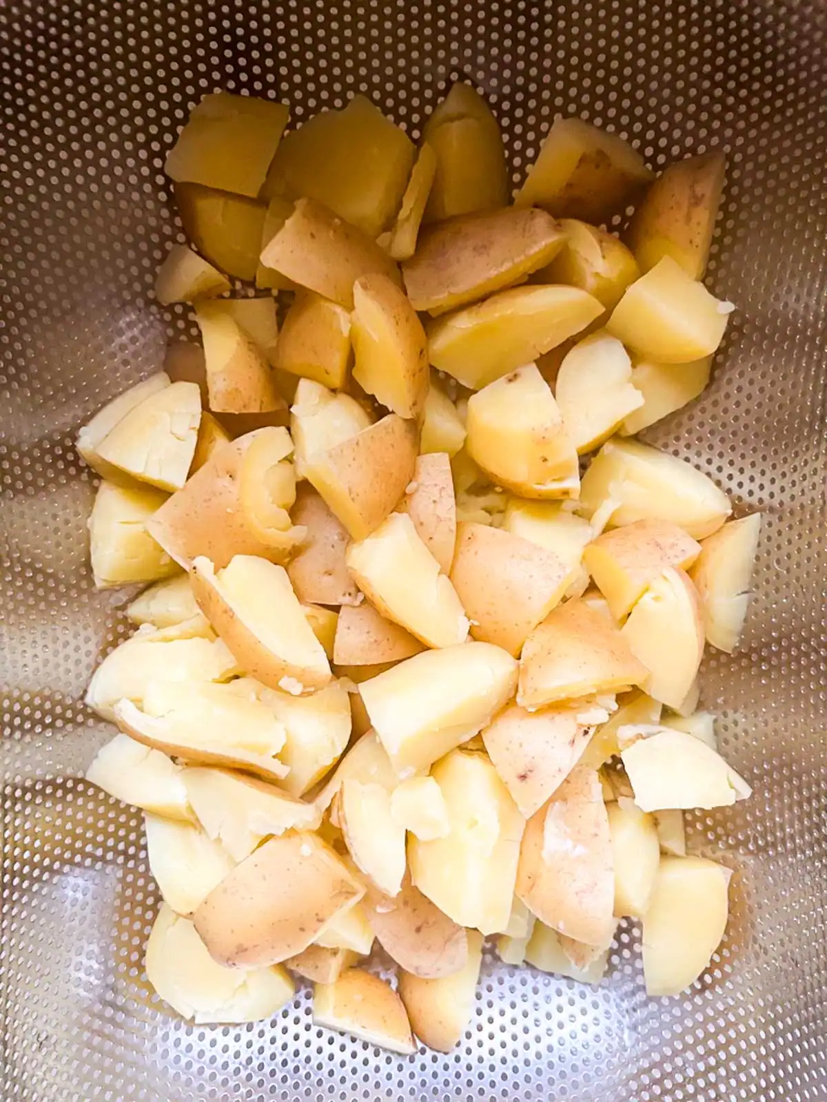 Cooked potato chunks in a colander.