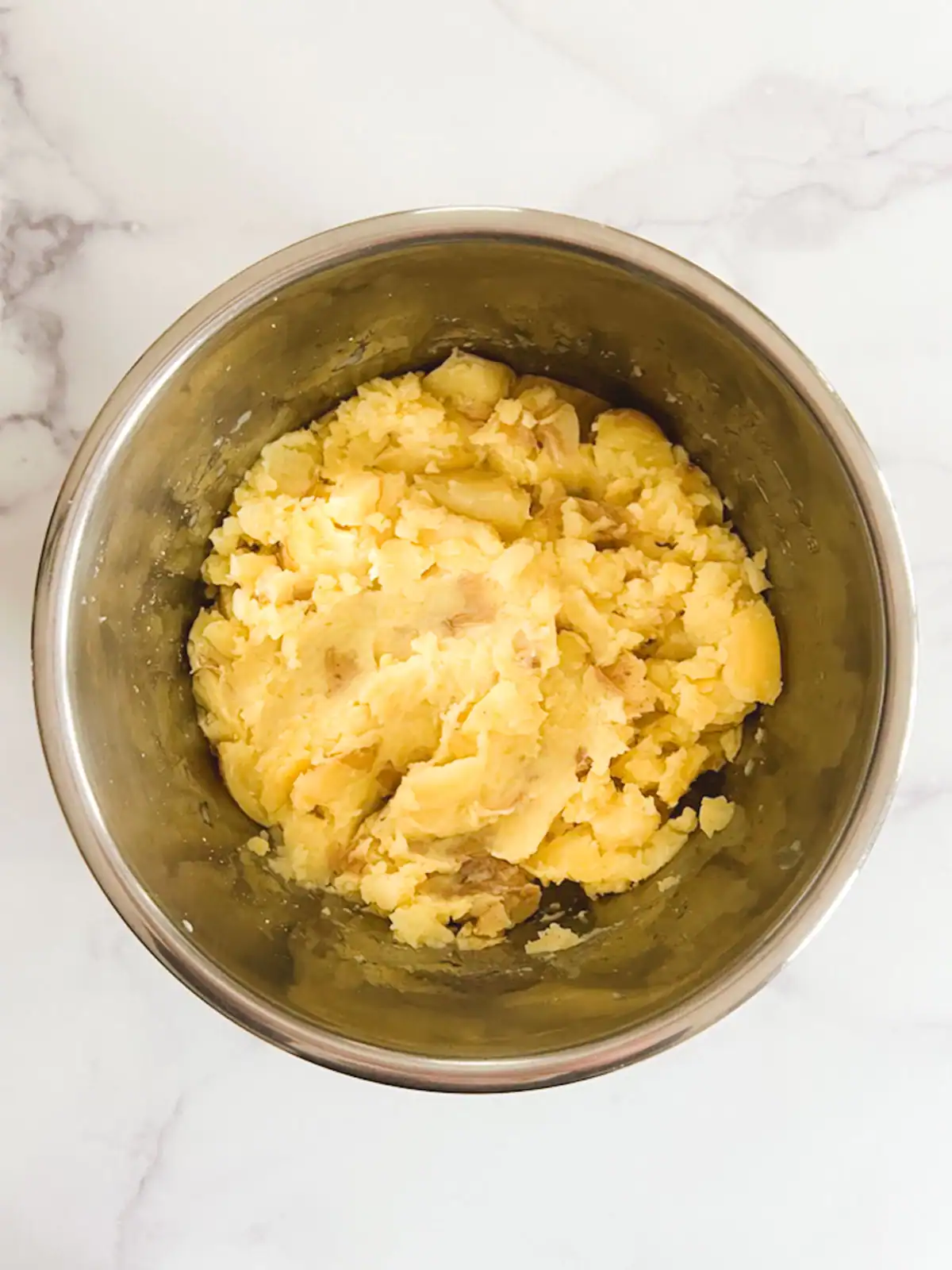 Creamy mashed potatoes in a stainless steel bowl on marble surface.