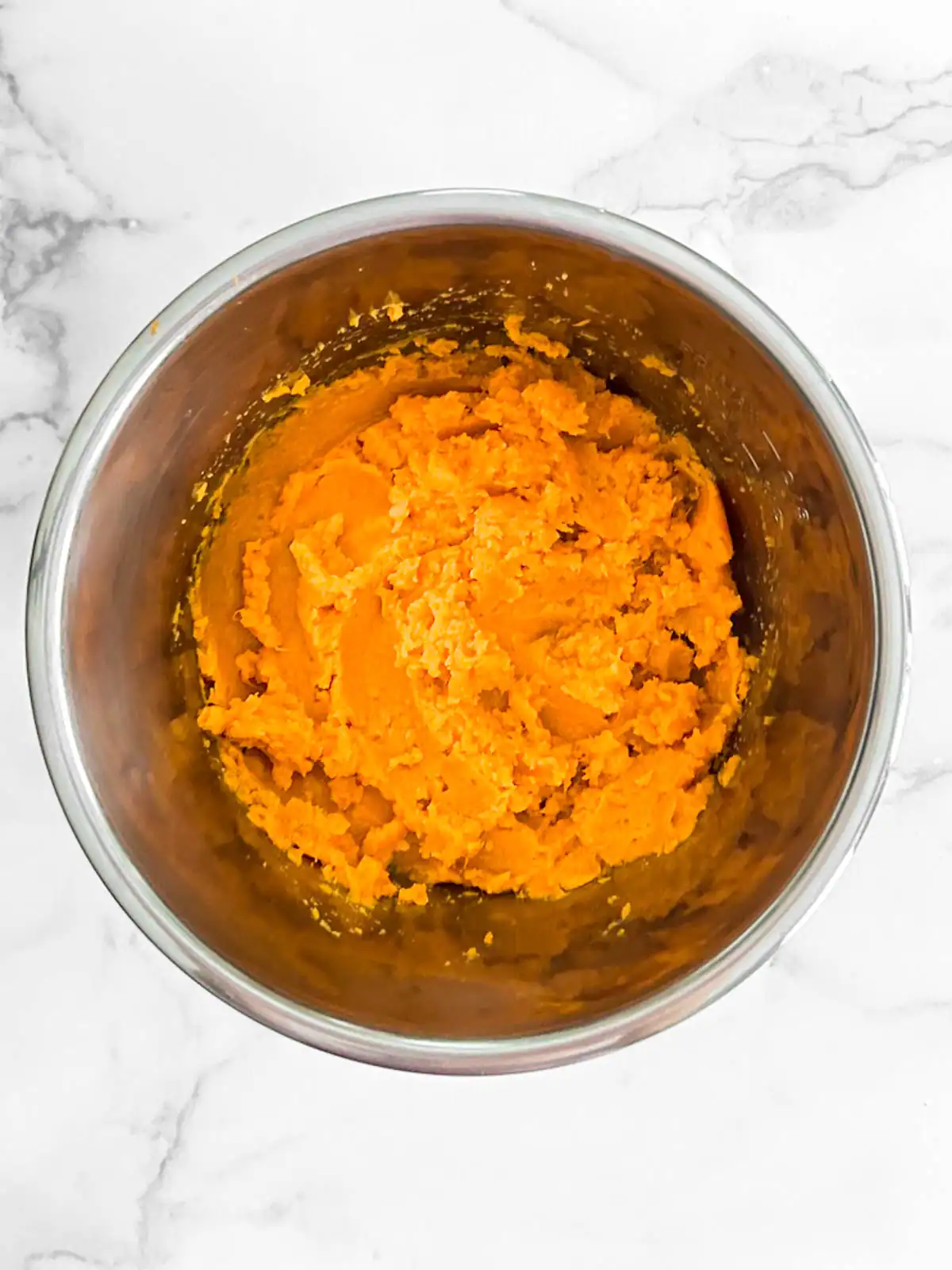 Creamy mashed sweet potatoes in a stainless steel bowl.