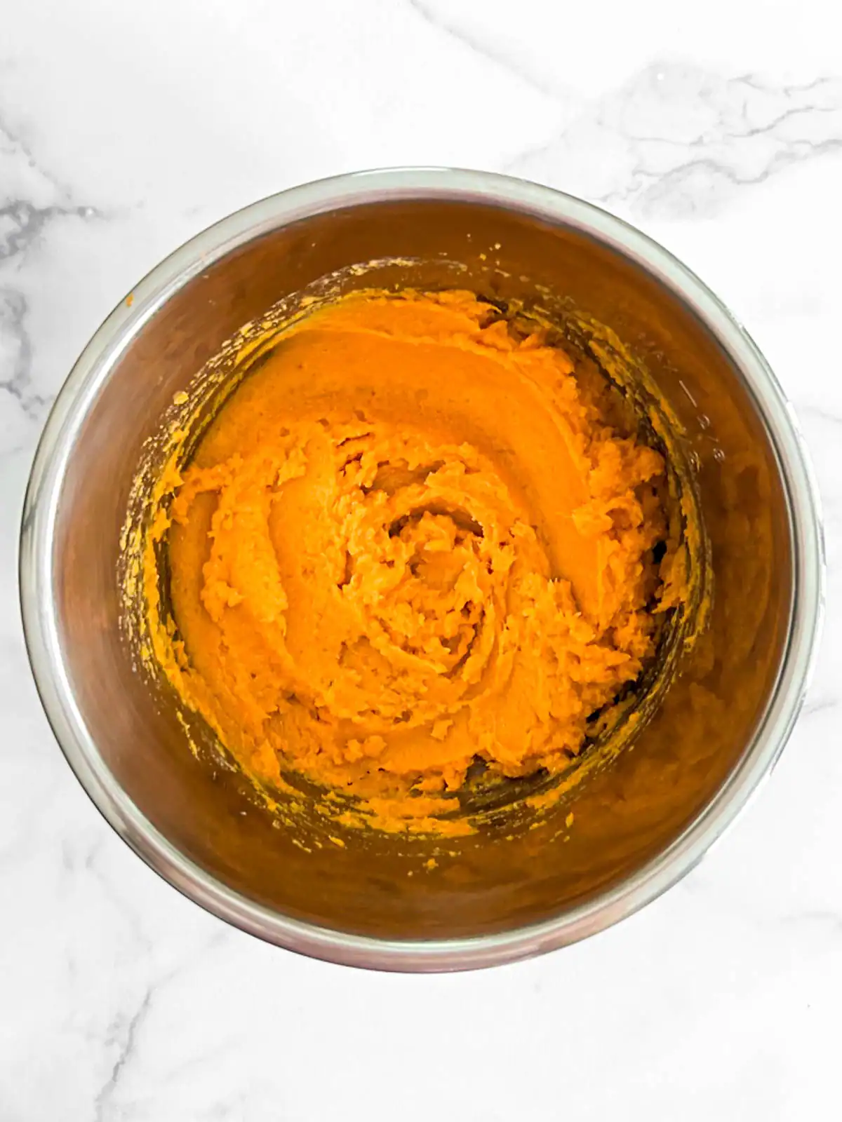 Creamy mashed sweet potatoes in a stainless steel bowl.