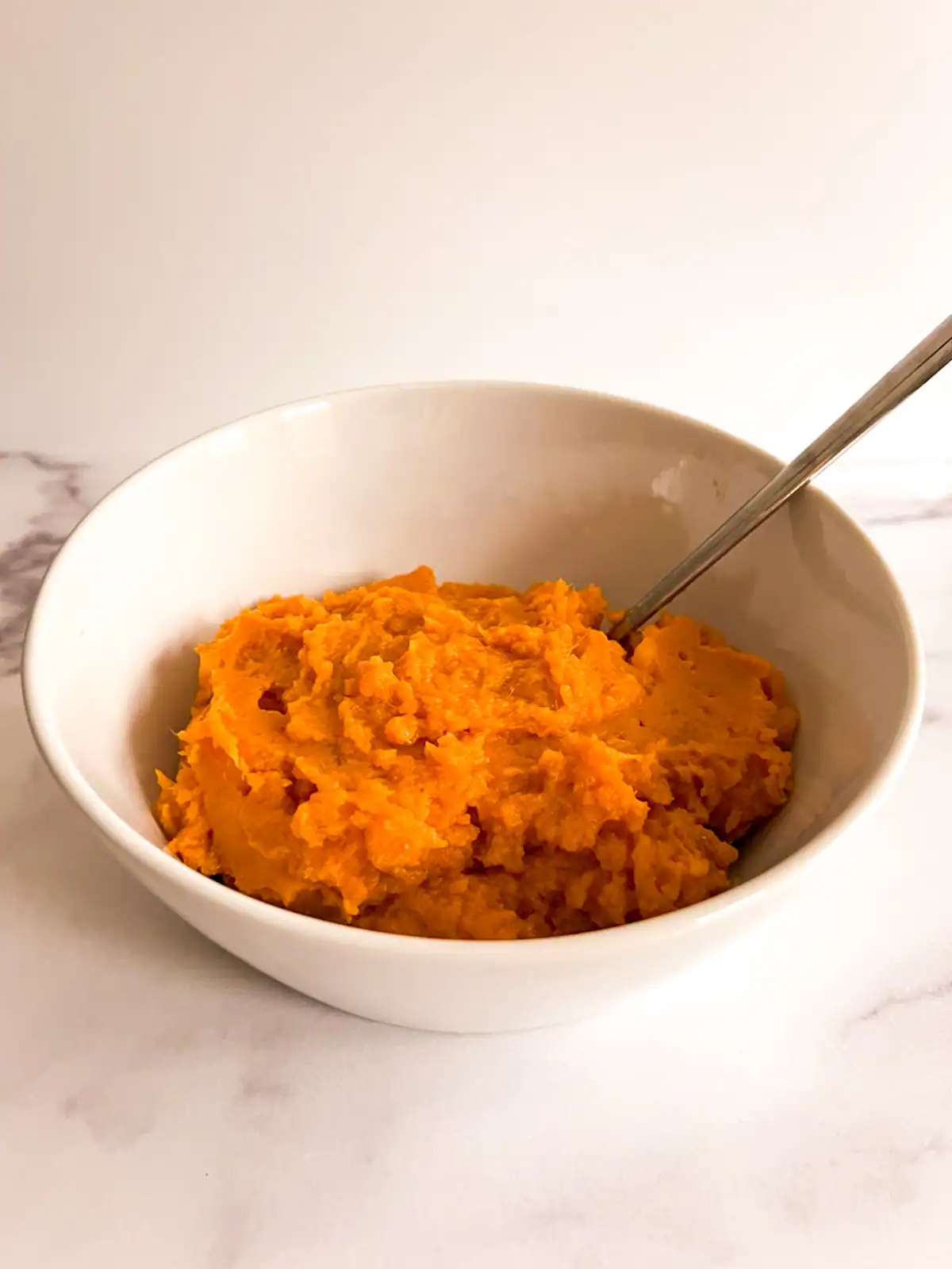Creamy mashed sweet potatoes in a white bowl on a marble surface.