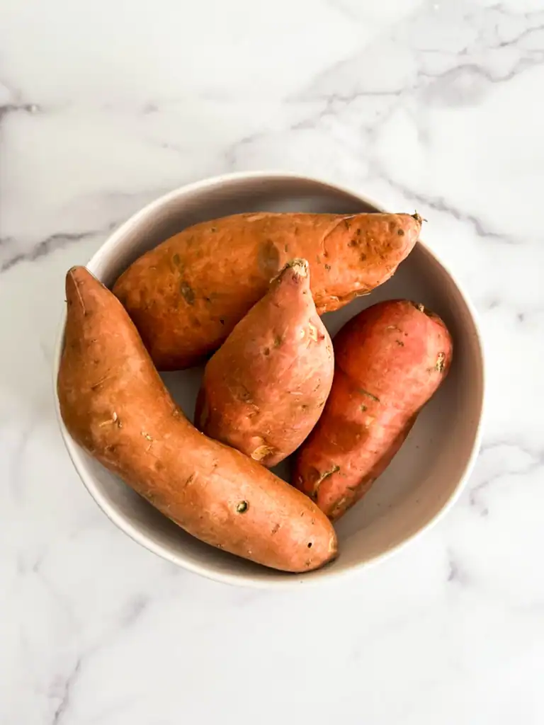Sweet potatoes in a white bowl on a marble surface.