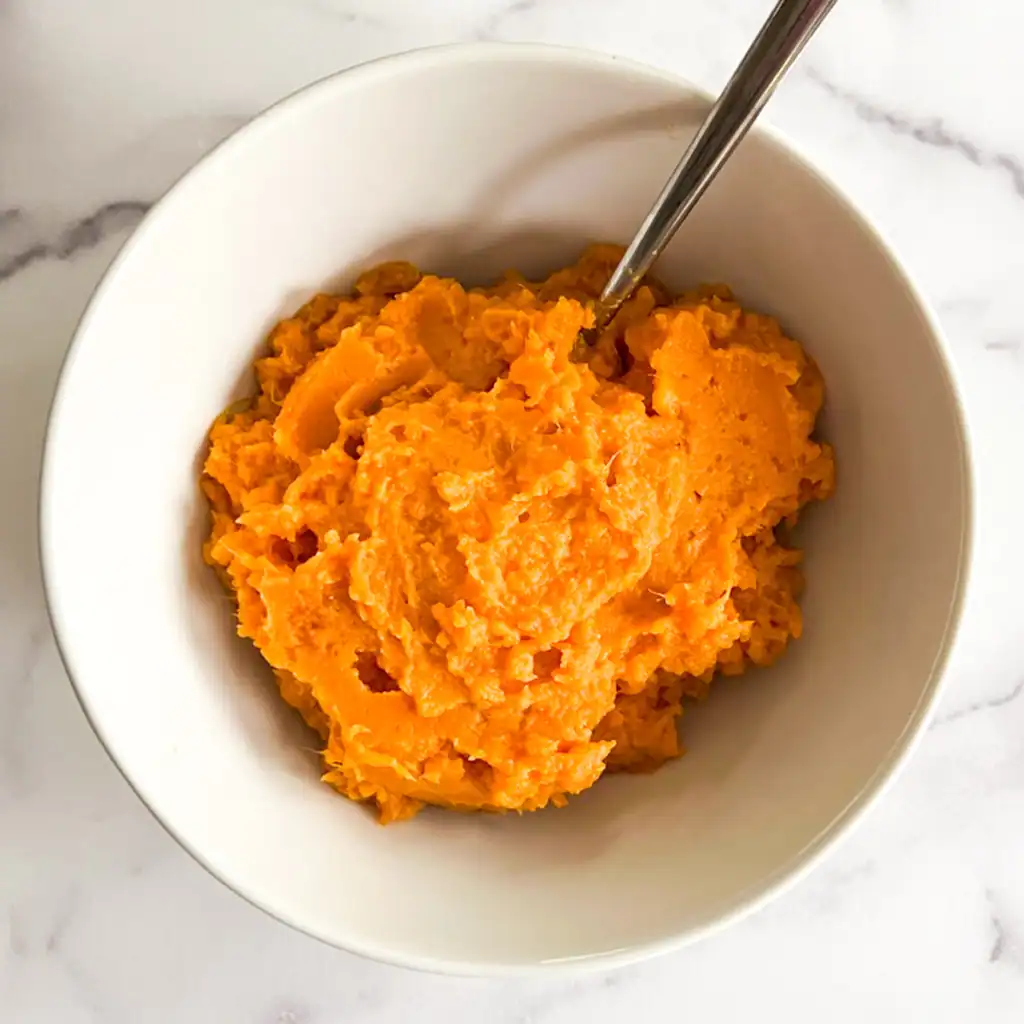 Creamy vegan mashed sweet potatoes in a white bowl on a marble background.