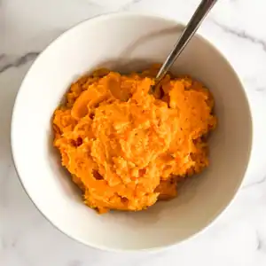 Creamy vegan mashed sweet potatoes in a white bowl on a marble background.