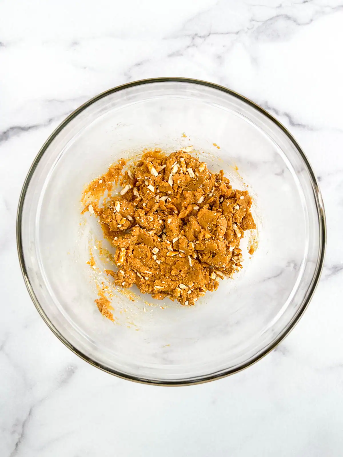 Peanut butter dough with chopped pretzels added in a glass bowl.