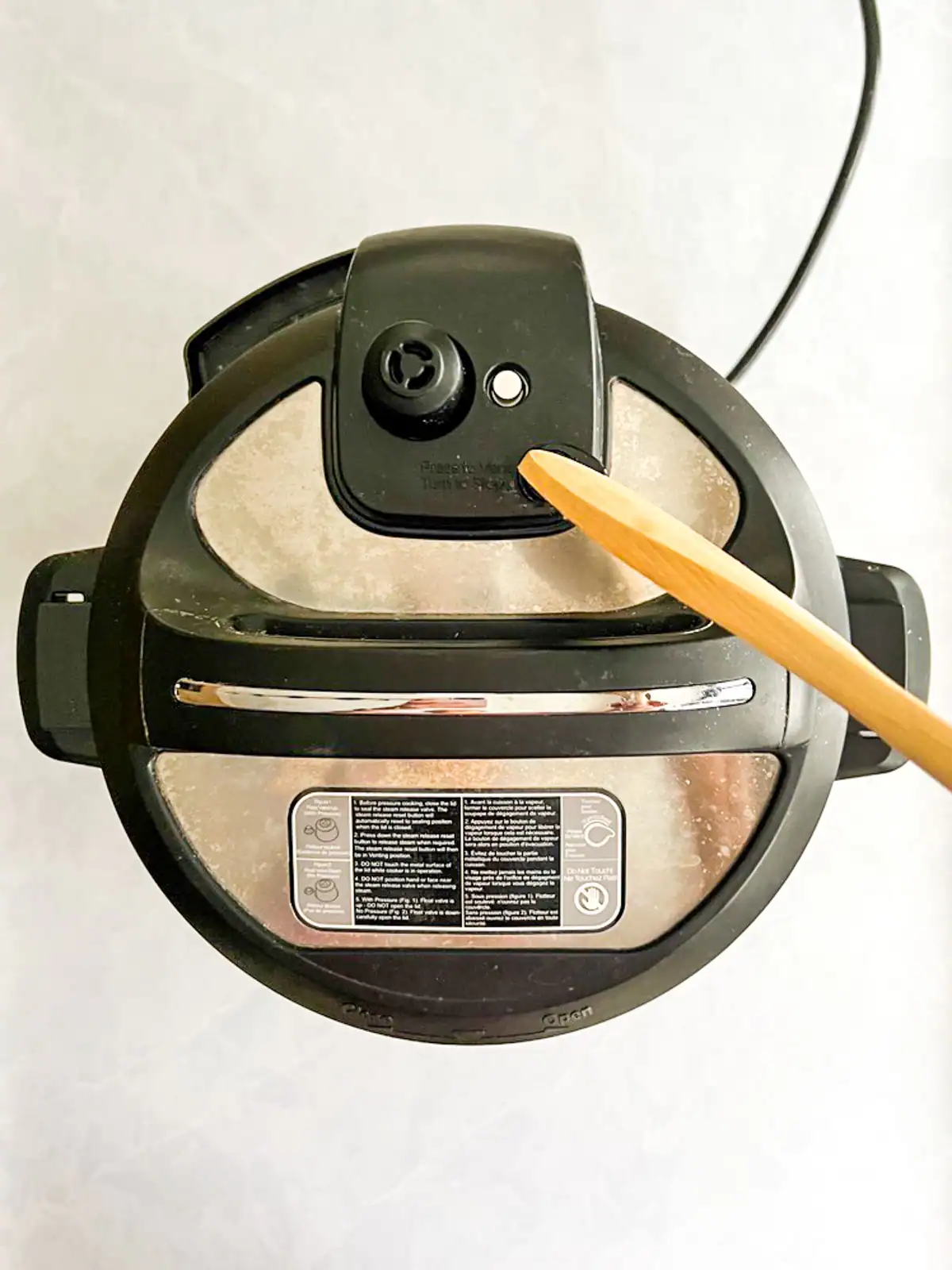 Wooden spoon adjusting the vent on an Instant Pot.