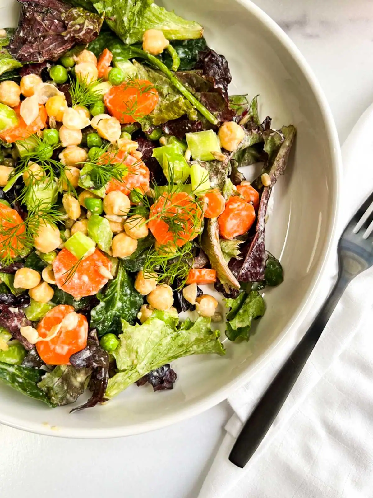 Chickpea veggie salad with vegan Caesar dressing in a white bowl.