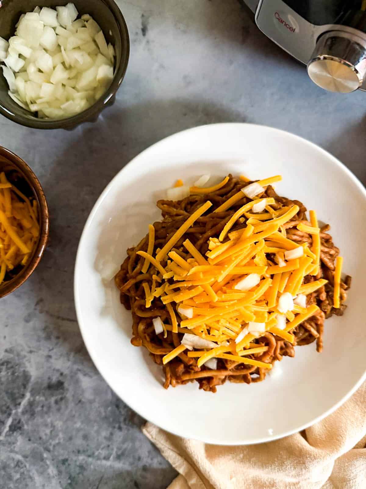 Instant Pot Cincinnati chili topped with shredded vegan cheese and diced onions.