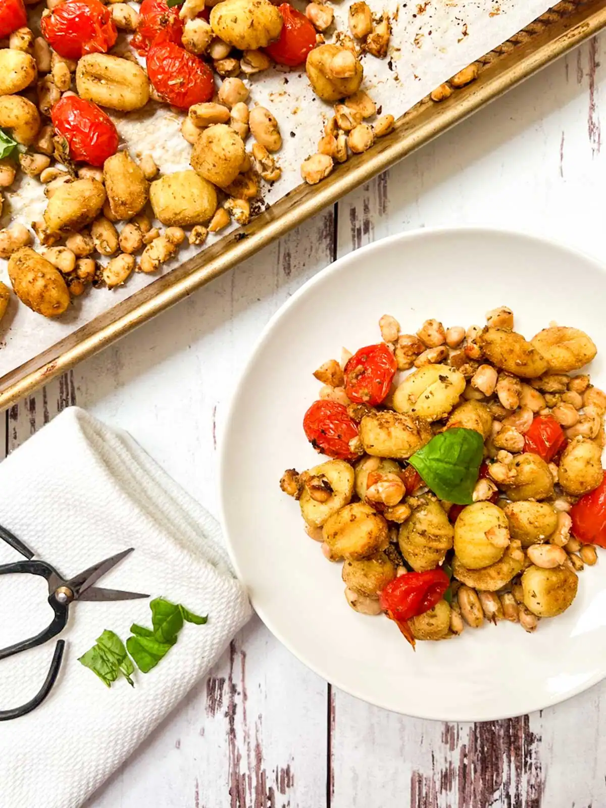Gnocchi with blistered tomatoes and white beans next to a sheet pan.