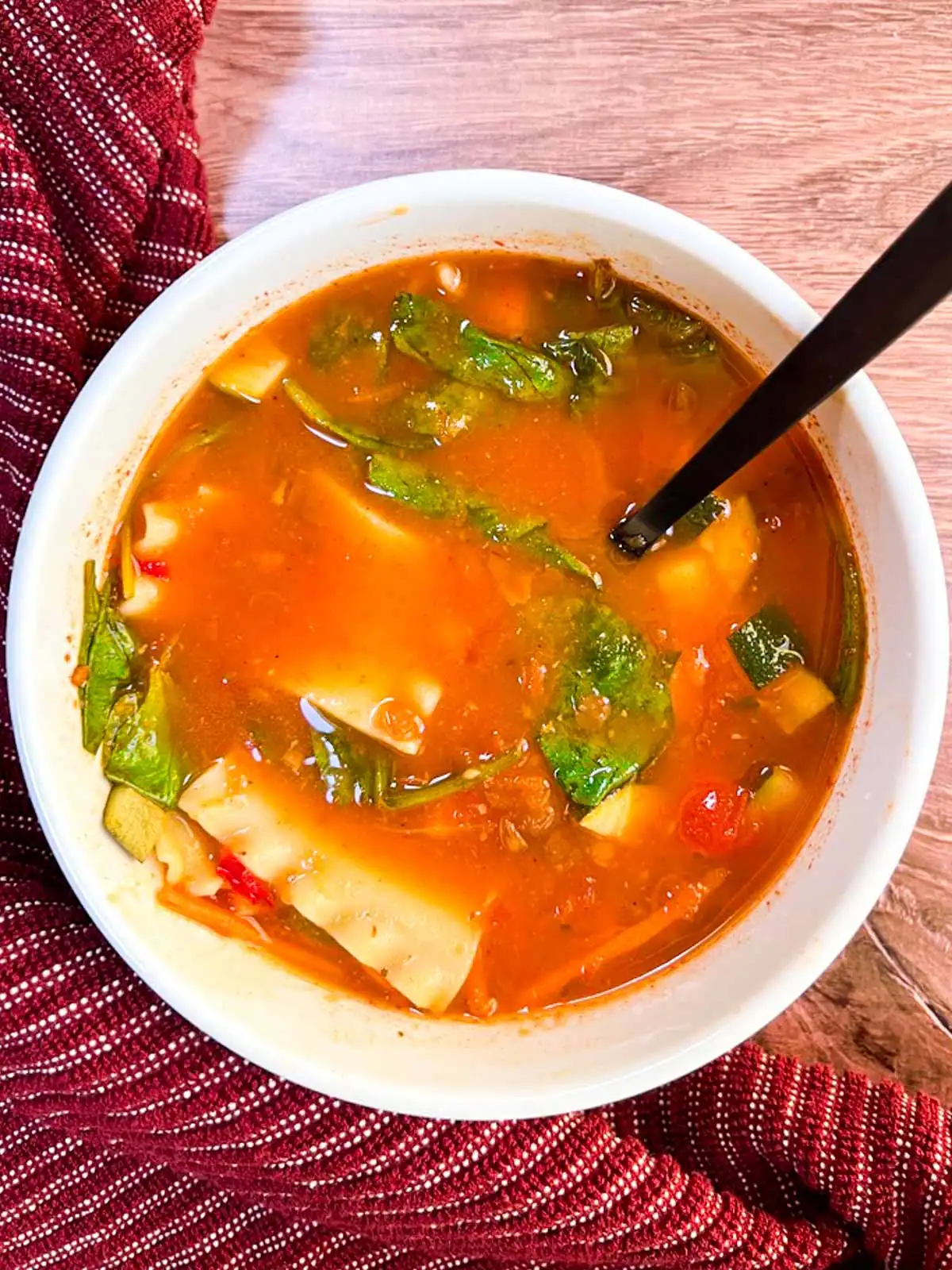 A bowl of spicy vegan lasagna soup on a wooden background.