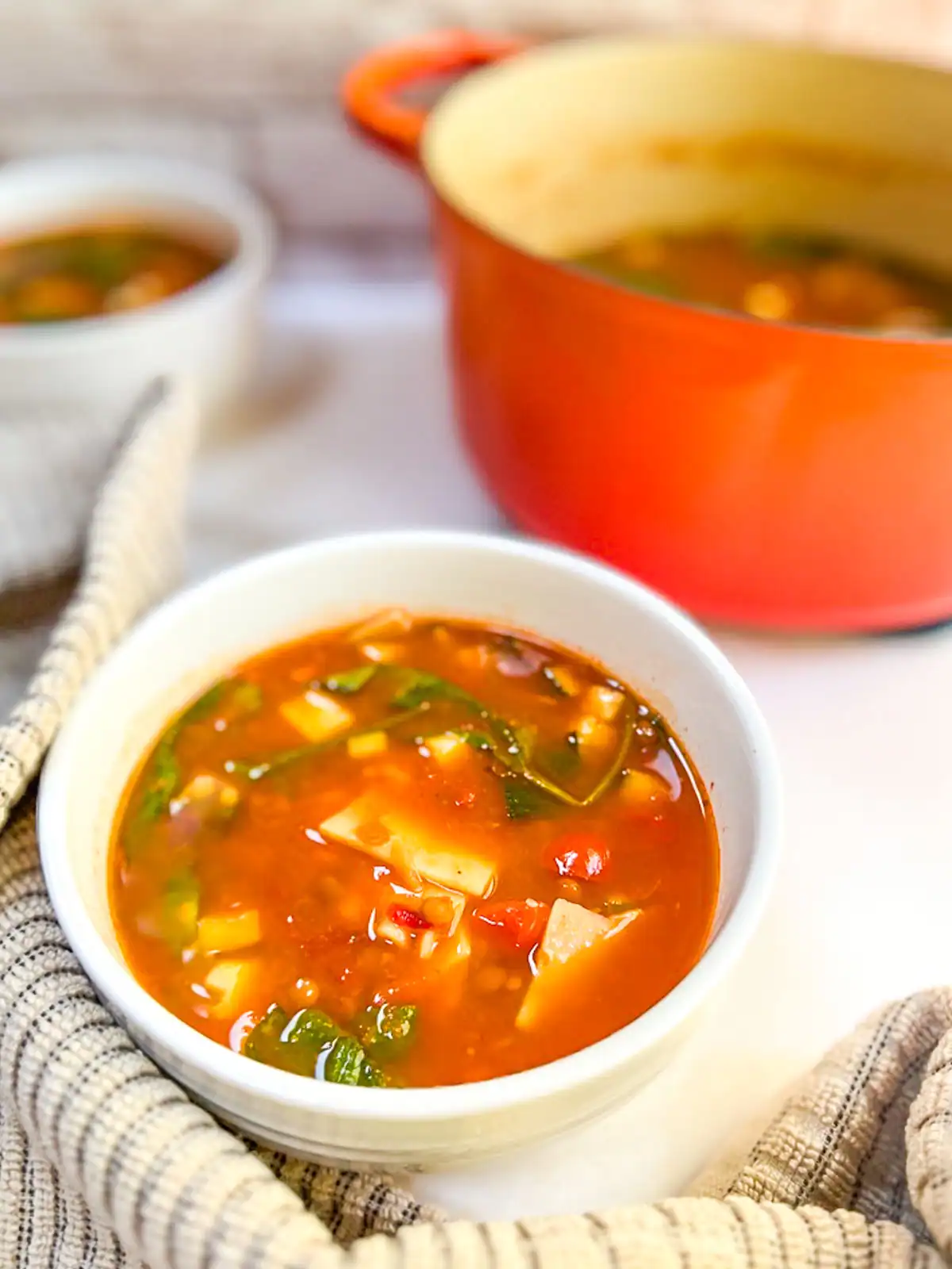A bowl of spicy vegan lasagna soup with a pot in the background.