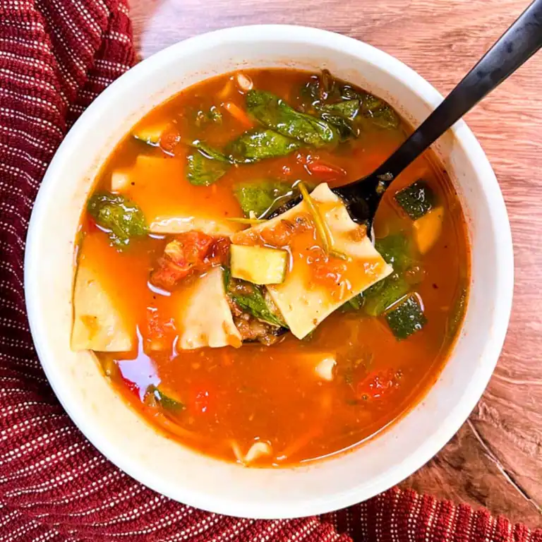 A bowl of spicy vegan lasagna soup on a wooden table.